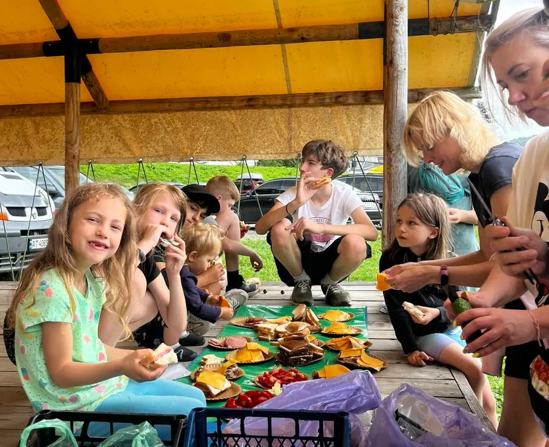 Children sharing lunch under a marquee at camp, one girl smiling at the camera
