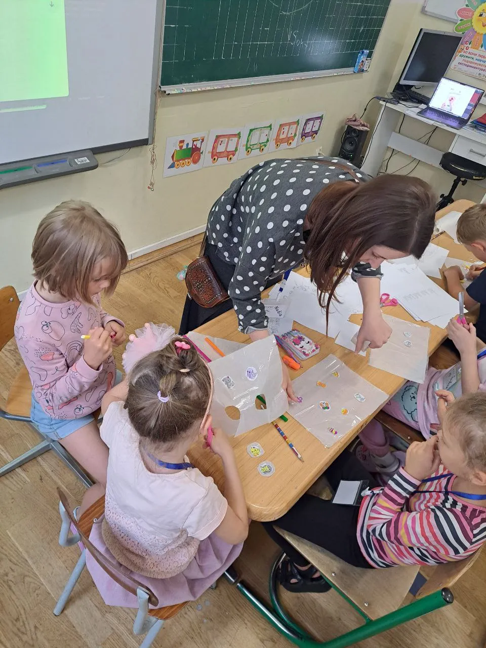 A volunteer leaning in to help children with a craft activity at a classroom table