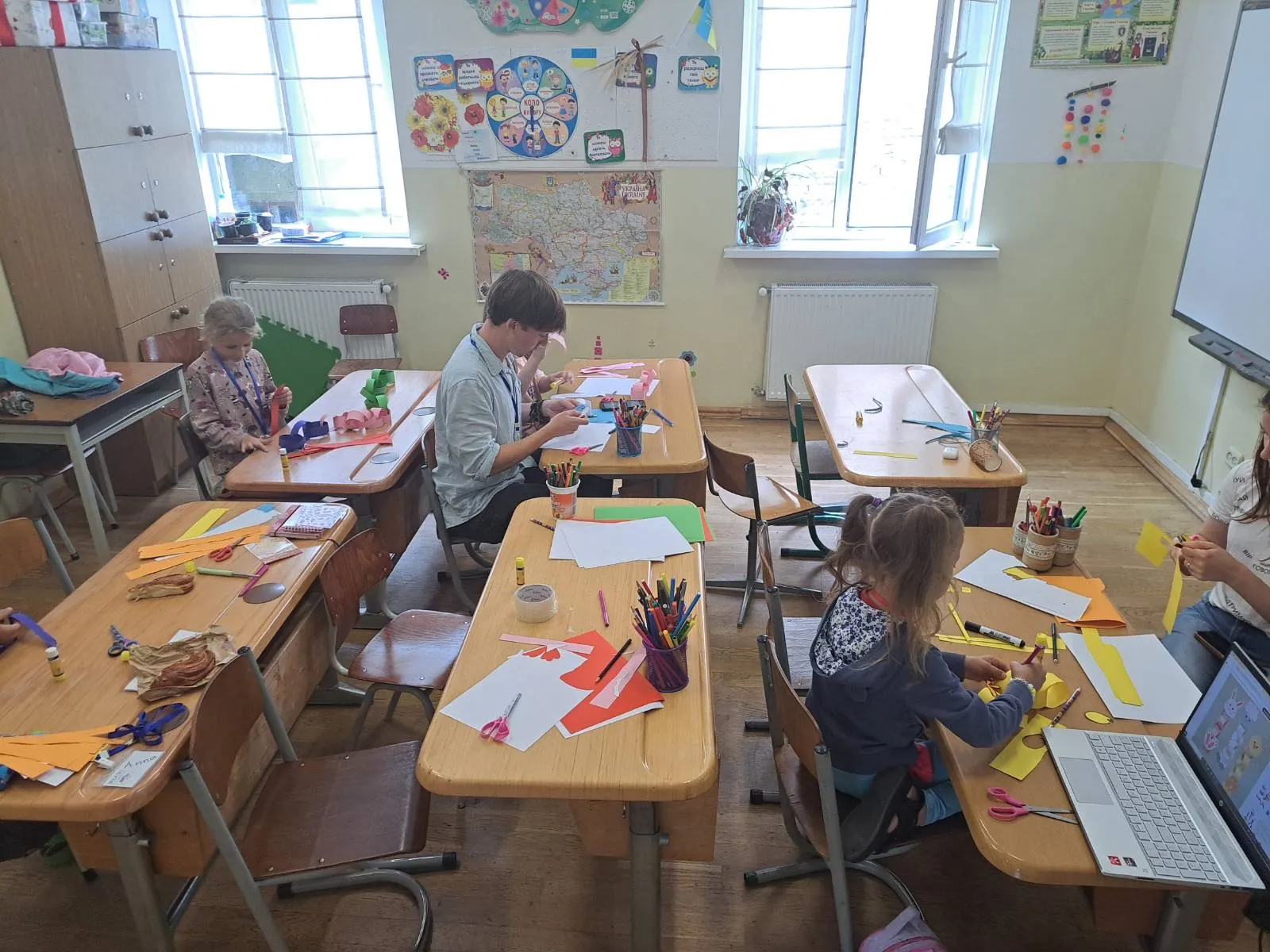 Children making paper crafts at desks in a bright classroom