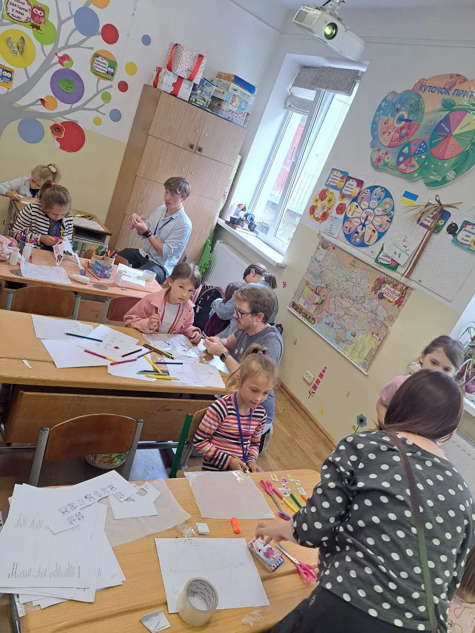 A volunteer guiding children through a hands-on session at their desks